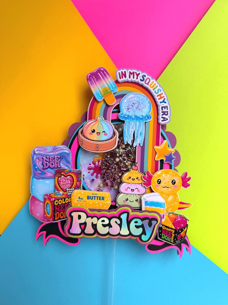 Puede incluir: Un adorno para tarta multicapa con el nombre Presley en fuente negrita, rodeado de recortes coloridos de un polo, una medusa, un ajolote y varias cajas de juguetes. El centro incluye un elemento tipo shaker con cuentas y el texto In My Squishy Era.