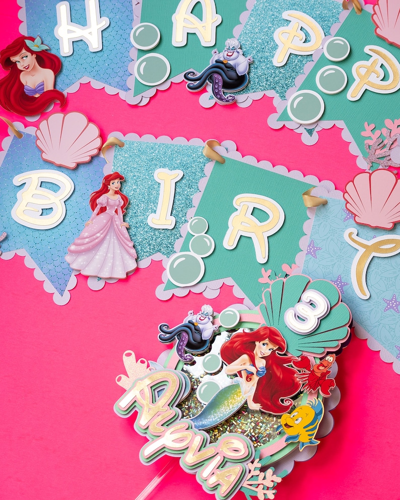 May include: A teal and white birthday banner with gold glitter and the words "Happy Birthday". The banner features Ariel, Ursula, and seashells. A separate topper features Ariel as a mermaid with the words "Happy Birthday" and the number "3" in a seashell.