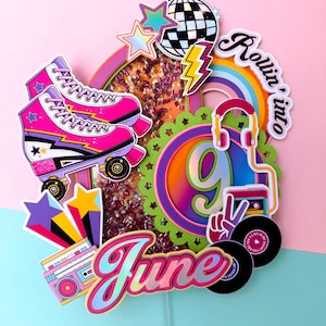 Peut inclure: Une décoration de gâteau multicouche avec un patin à roulettes rose, une boule à facettes, un éclair, un arc-en-ciel, un casque, un lecteur cassette et des disques vinyles. Le centre affiche le chiffre 9 et le nom June en écriture cursive.