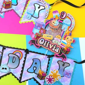 Puede incluir: Un conjunto de bander&iacute;n de cumplea&ntilde;os y adorno para pastel con fondo de galaxia y bordes festoneados. El bander&iacute;n deletrea HAPPY BIRTHDAY con letras coloridas. El adorno muestra el nombre Olivia, el n&uacute;mero 9 y varios gr&aacute;ficos de juguetes.