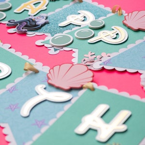 May include: A teal and pink banner with gold letters spelling out "Happy" and a seashell, mermaid, and seahorse design.