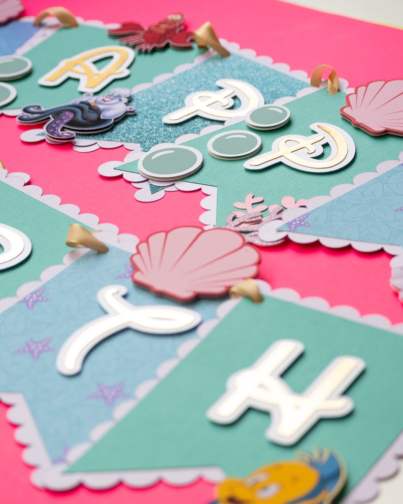 May include: A teal and pink banner with gold letters spelling out "Happy" and a seashell, mermaid, and seahorse design.