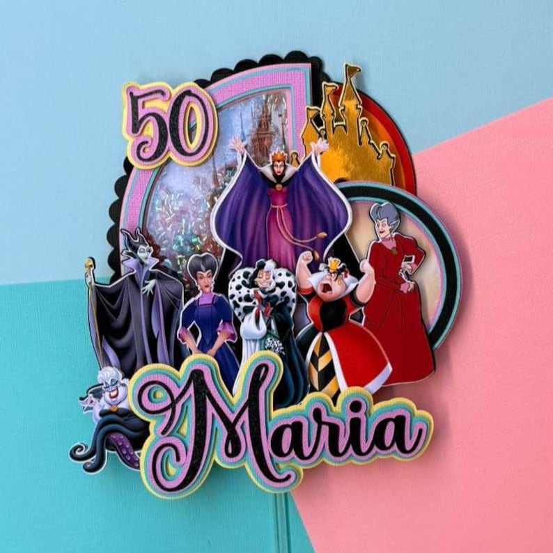May include: A colorful cake topper featuring Disney villains, the number 50, and the name "Maria". The design includes images of a castle and various characters in shades of purple, red, and black, set against a pink and blue background.