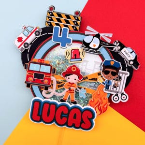 May include: A colorful birthday cake topper with a fire truck, ambulance, police car, helicopter, and a firefighter and police officer. The number 4 and the name "LUCAS" are also included. The background is red, yellow, and blue.