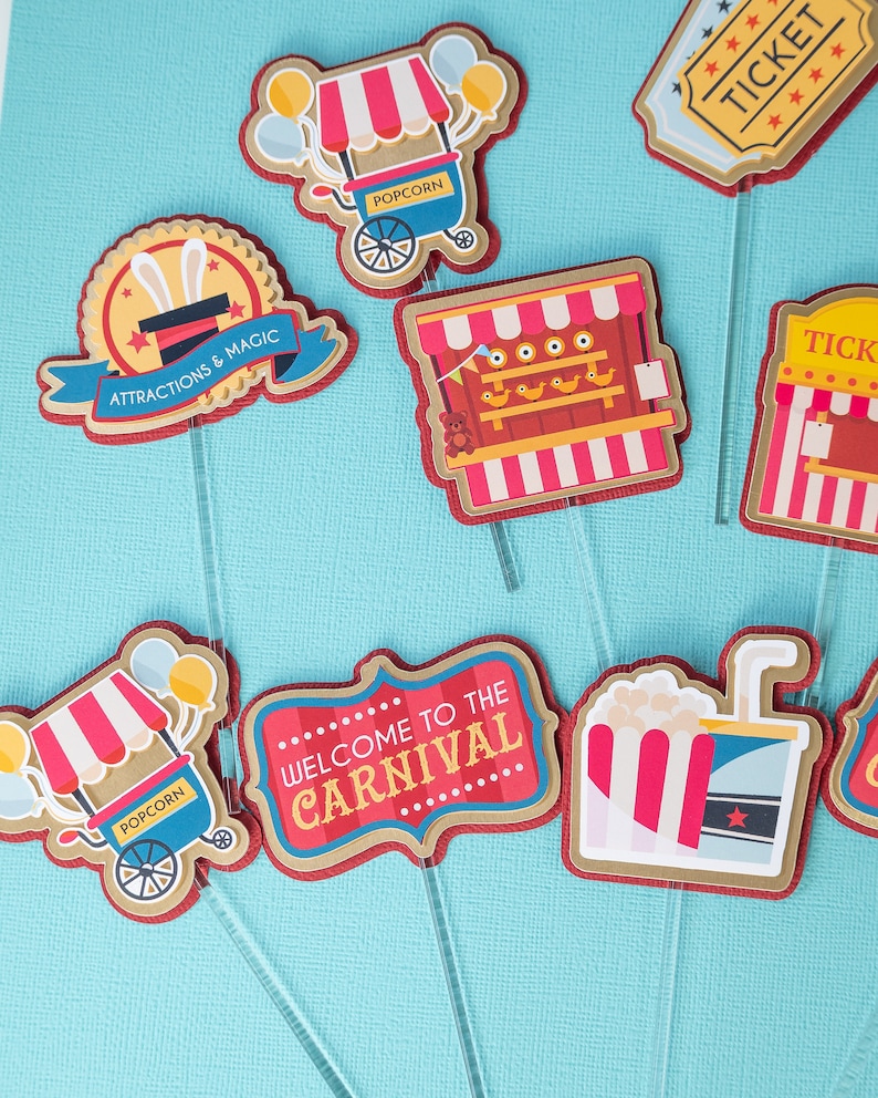 May include: A set of 8 carnival themed cupcake toppers. The toppers feature images of popcorn stands, a ticket booth, a shooting gallery, a magic show, and a welcome to the carnival sign. The toppers are printed on cardstock and have red, white, and blue accents.