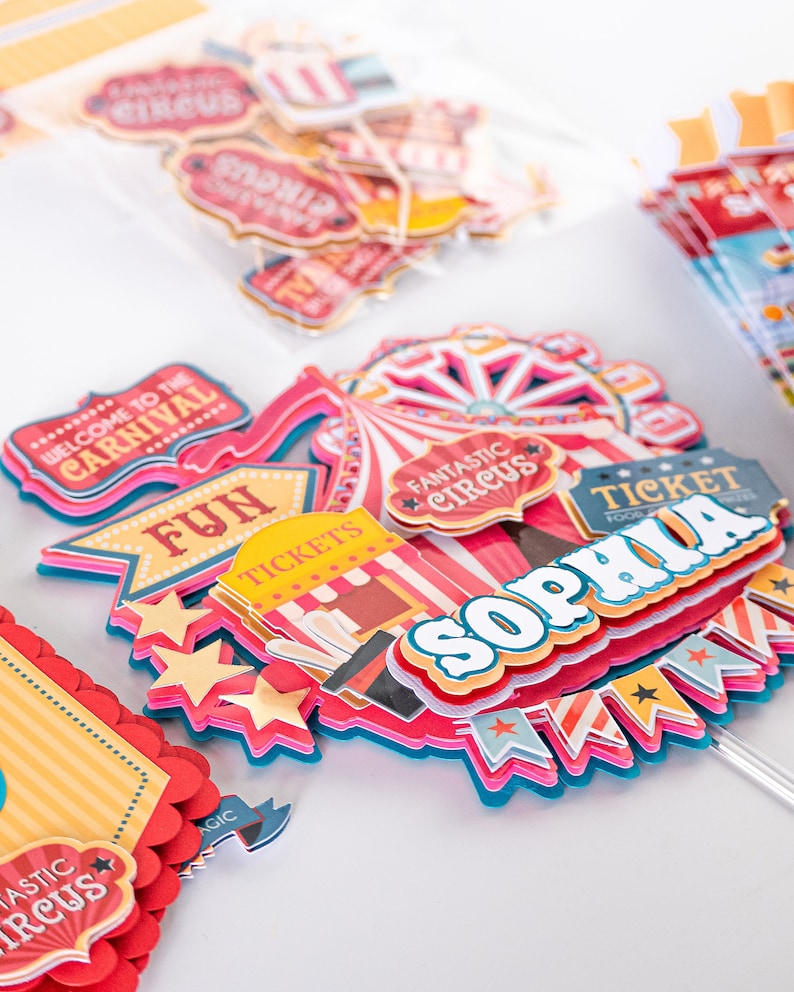 May include: A colorful set of circus-themed cake toppers with the words "Welcome to the Carnival", "Fun", "Tickets", "Fantastic Circus", "Ticket", and "Sophia".