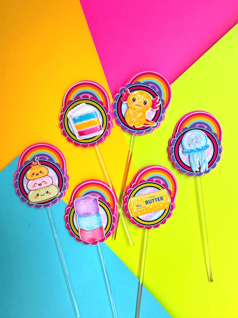 Puede incluir: Seis adornos decorativos para cupcakes sobre palitos de pl&aacute;stico transparente, cada uno con borde festoneado, un arco&iacute;ris y una ilustraci&oacute;n &uacute;nica que incluye un pastel en capas, un ajolote, una medusa, dumplings, malvaviscos y mantequilla.