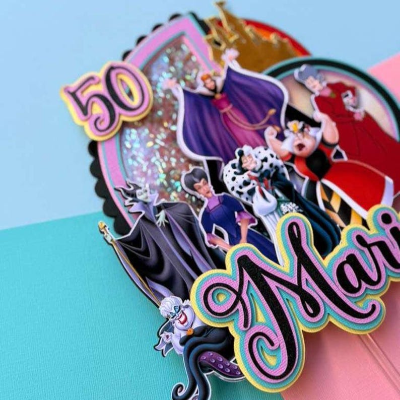 May include: A colorful cake topper featuring cartoon villains, the number 50, and the name "Mari". The topper includes images of Ursula, Maleficent, the Evil Queen, and Cruella de Vil. The design has a pink, blue, and black color scheme.
