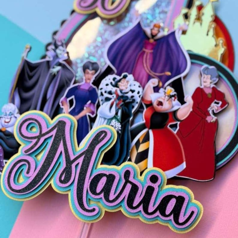 May include: A colorful cake topper featuring cartoon villains. The name "Maria" is displayed in a layered, cursive font with black, pink, and blue accents. The background includes images of a castle and other decorative elements.