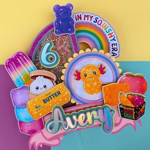 Może przedstawiać: Kolorowa dekoracja na tort z elementem typu shaker z cyfrą 6, fioletowym żelkowym misiem, tęczą z napisem IN MY SQUISHY ERA, aksolotlem, lodem na patyku, pierożkiem, kostką masła oraz tabliczką z imieniem Avery.