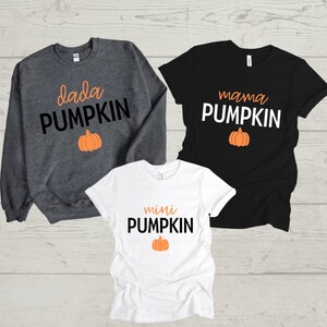 Puede incluir: Tres camisetas con un tema de calabaza. La primera camiseta es gris y dice "dada pumpkin" con un pequeño gráfico de calabaza naranja. La segunda camiseta es negra y dice "mama pumpkin" con un pequeño gráfico de calabaza naranja. La tercera camiseta es blanca y dice "mini pumpkin" con un pequeño gráfico de calabaza naranja.