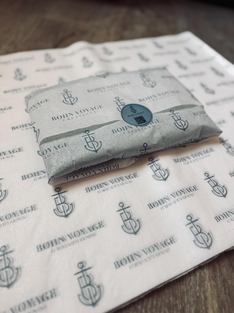 May include: A wrapped package on patterned paper. The paper features a repeating anchor and the text "BOHN VOYAGE CREATIONS". A round sticker with the same logo seals the package. The background is a light wood grain.