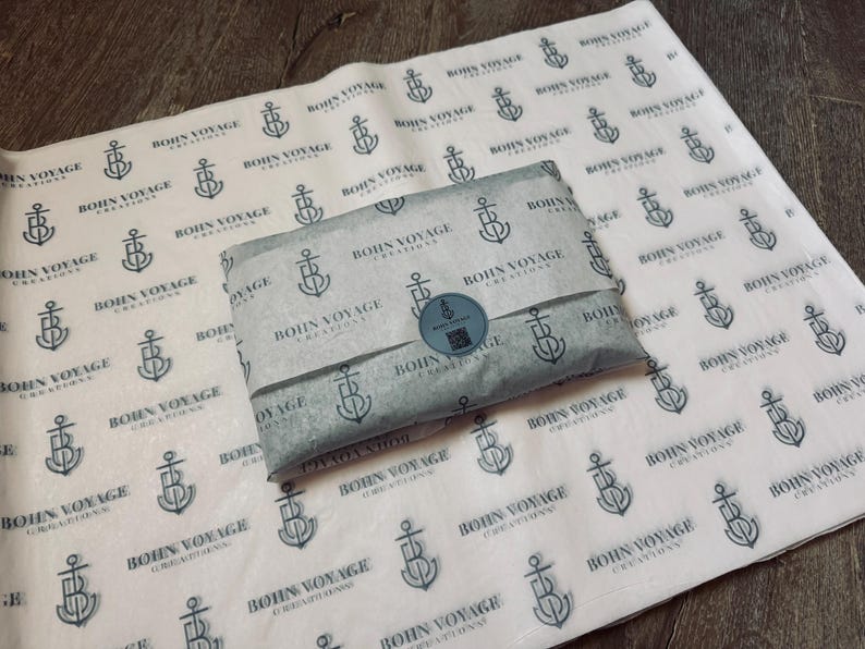 May include: A package wrapped in gray tissue paper with a repeating pattern of anchors and the text "Bohn Voyage Creations." A round sticker seals the package. The tissue paper is laid on a larger sheet with the same design.