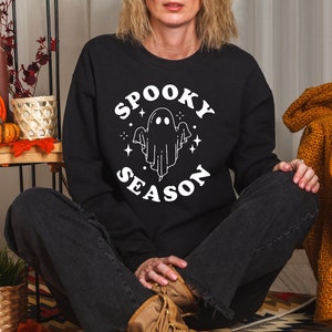 Può includere: Felpa nera con la scritta "Spooky Season" in un design circolare, con un'illustrazione di un fantasma bianco. Questa felpa a tema Halloween è un articolo stagionale.