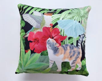 May include: Square decorative pillow with a vibrant tropical design. The pillow features a calico cat, red hibiscus flowers, a hummingbird, and a light blue butterfly against a black background with green foliage.