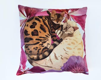 Peut inclure: Un coussin décoratif avec une illustration aquarelle de deux chats dormant sur un lit de fleurs roses et violettes.