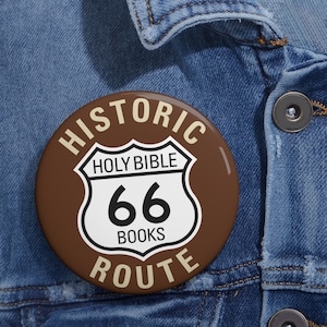 May include: A brown button with a white Route 66 sign that says "Holy Bible 66 Books" and the words "Historic Route" around the sign.