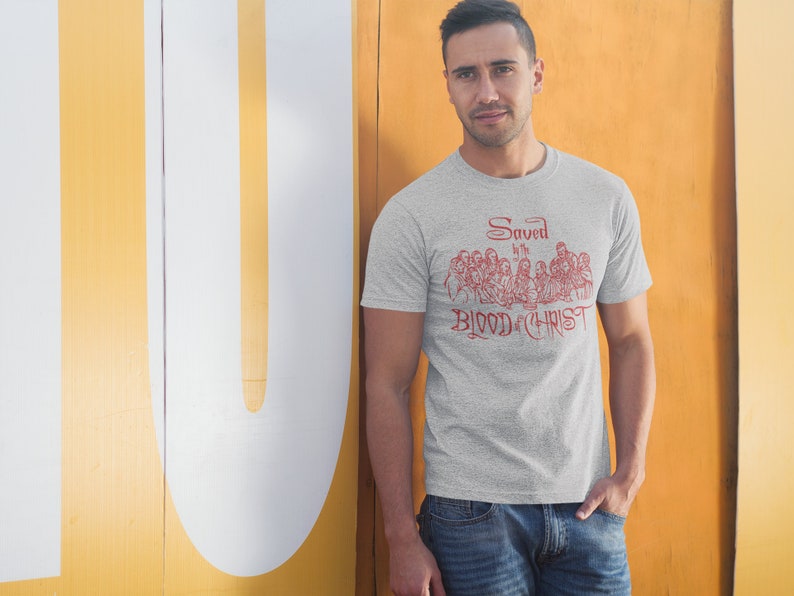 May include: A heather grey t-shirt featuring a red graphic of a group of people seated at a table. The graphic includes the text "Saved by the Blood of Christ".