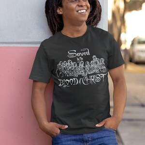 May include: A black t-shirt featuring a white graphic of the Last Supper and the text "Saved by the Blood of Christ".