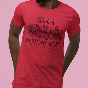 May include: Red t-shirt featuring a black graphic of the Last Supper and the text "Saved by the Blood of Christ".