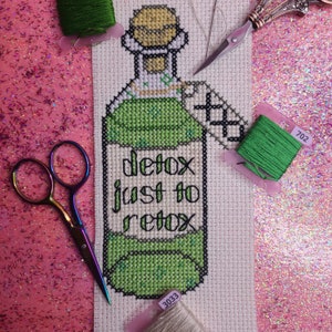 Peut inclure: Modèle de point de croix d'une bouteille en verre verte avec le texte "detox just to retox" sur fond blanc. L'image comprend différentes couleurs de fil à broder dans des contenants en plastique.