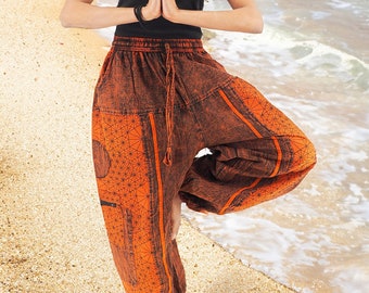 Puede incluir: Una mujer con pantalones impresos de color naranja y marrón con un diseño geométrico. Está de pie en una playa de arena con el océano de fondo.