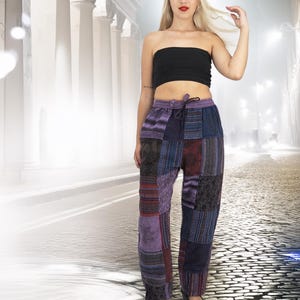 May include: Purple patchwork trousers with a drawstring waist. The trousers feature a variety of different patterns and colours, including purple, blue, red, and black. The trousers are made from a soft, comfortable fabric.