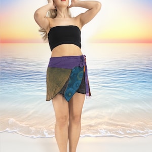 May include: A woman wearing a black bandeau top and a multi-coloured wrap skirt with a floral pattern. She is standing on a white sandy beach with blue water in the background.