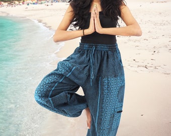 May include: A woman wearing blue printed pants with a black tank top, standing on one leg in a yoga pose on a sandy beach.