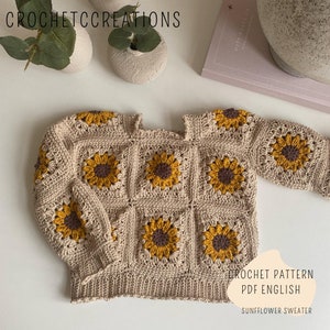 May include: Crochet pattern PDF in English for a sunflower sweater. The sweater is beige with yellow and brown sunflower motifs.