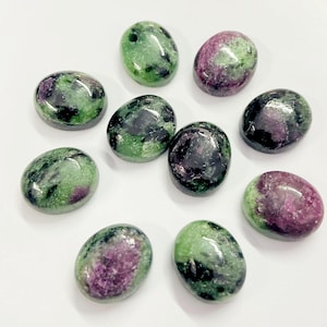 May include: Ten oval-shaped green and pink gemstones with black flecks. The stones are smooth and polished.