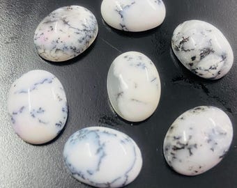 Op de afbeelding: Zeven ovale witte edelstenen met zwarte en grijze dendritische patronen. De gepolijste stenen hebben een glanzende afwerking. De edelstenen zijn gerangschikt op een donkere ondergrond, wat hun natuurlijke schoonheid benadrukt.