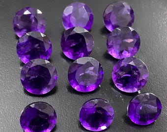 Könnte beinhalten: Eine Ansammlung von elf runden, facettierten Amethyst-Edelsteinen. Die tiefvioletten Edelsteine sind eng angeordnet. Die Facetten erzeugen einen funkelnden Effekt, der das Licht reflektiert. Geeignet für Schmuckherstellung oder Sammlungen.