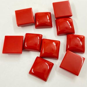 May include: A collection of vibrant red square-shaped beads. The beads have a glossy finish and rounded edges. They are scattered across a white surface, showcasing their bright color and smooth texture. These beads are ideal for jewelry making.