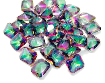 May include: A pile of iridescent, square-cut rhinestones. The gems display a spectrum of colors, including green, purple, and blue, with a reflective, polished surface. The rhinestones are scattered, creating a sparkling effect.