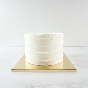 May include: A white cake with a smooth, white frosting on a gold cake board.