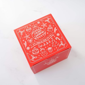 May include: A red square gift box with a white illustrated design featuring Christmas ornaments, a snowman, a Christmas tree, and the text "MERRY CHRISTMAS" and "Best wishes for Happy New Year!"