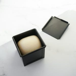Ball of dough in a black container on a white surface