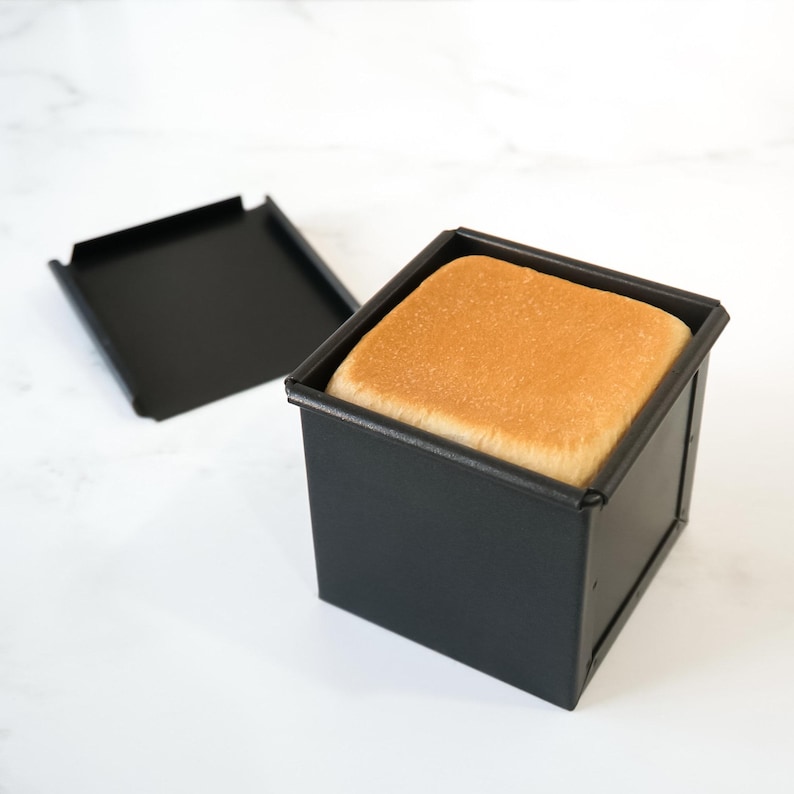 Square piece of bread in a black loaf pan on a white background