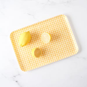 May include: A yellow and white gingham tray with three lemons on it. Two lemons are whole and one is cut in half.