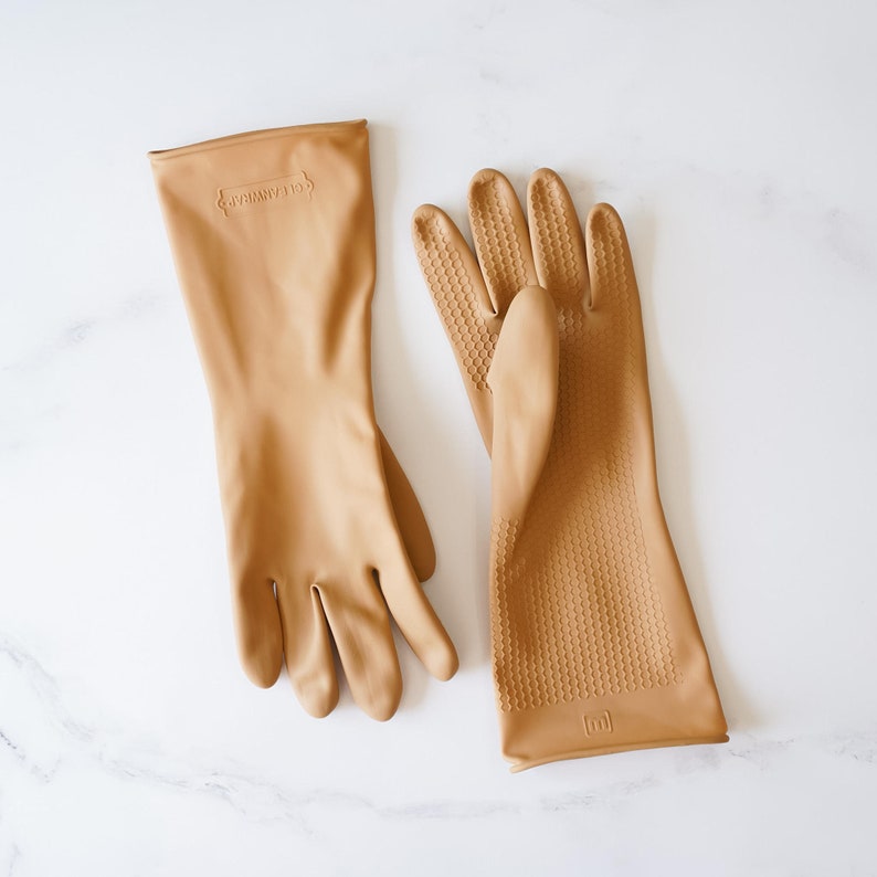 May include: Two pairs of tan rubber gloves. One pair has a textured surface and the other pair is smooth. The gloves have the text "Clean Mama" printed on the cuff.