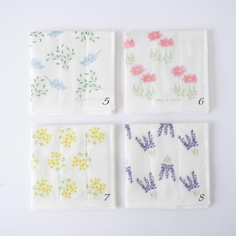 Four square white fabric kitchen cloths with different floral prints arranged in a 2x2 grid on a white background. The top-left cloth has blue flowers and green leaves, the top-right has pink flowers, the bottom-left has yellow flowers, and the bottom-right has purple lavender sprigs.