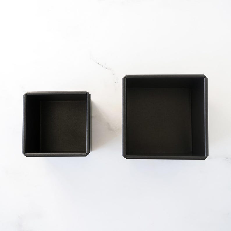 Two black square bread loaf pans on a white background