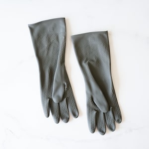 May include: A pair of gray rubber dishwashing gloves with a textured surface. The gloves have a logo on the back that says "WM".
