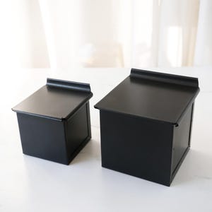 Two black metal bread loaf pans on a white surface with a neutral background