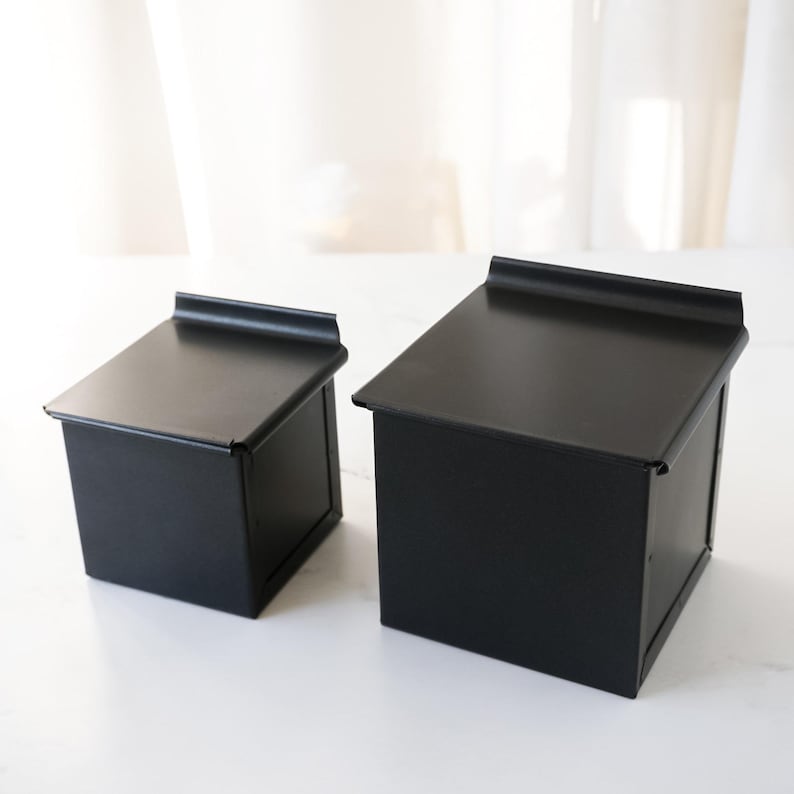 Two black metal bread loaf pans on a white surface with a neutral background