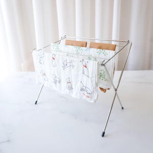 May include: A silver metal drying rack with four white cloth towels hanging on it. The towels have a pattern of small black dogs with red collars. The rack is on a white marble surface.