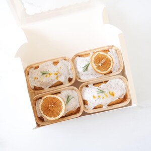 Four small dessert boxes with white glaze, orange slices, and green leaves on a white background.