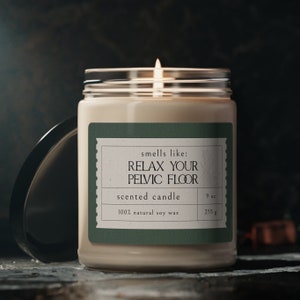 May include: A green and white scented candle with the text "smells like: RELAX YOUR PELVIC FLOOR" and "scented candle". The candle is in a clear glass jar with a lid and is 9 oz (255 g).