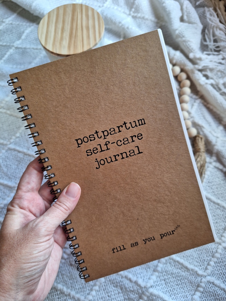May include: A brown spiral bound journal with the text "postpartum self-care journal" and the words "fill as you pour" at the bottom.
